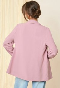 Roza blazer s prilagojenim krojem, z zareznimi reverji, dvema stranskima žepoma in gladko teksturo. Nosite ga čez svetlo modre kavbojke.