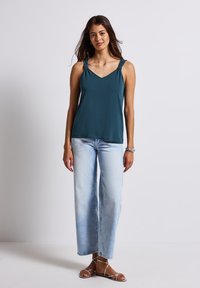 Teal ärmlös topp med V-ringning och knutna axelremmar, tillsammans med ljusblå vida jeans och sandaler med remmar.