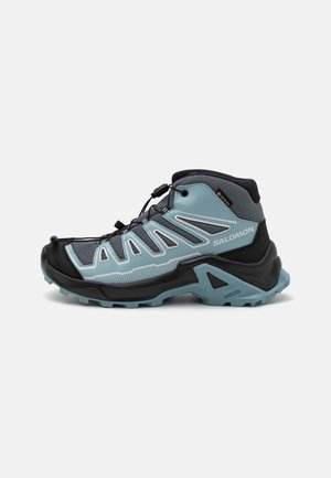 Shoe de caminhadas de cano médio com um design preto e azul claro, parte superior em malha, biqueira em borracha e padrão de sola agressivo.