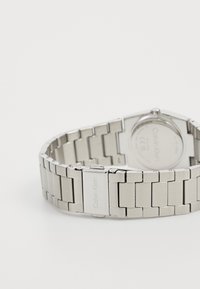 Sølv rustfritt stål armbåndsur med sekskantet kasse, lenkedesign og gravert merkevare på låsen.