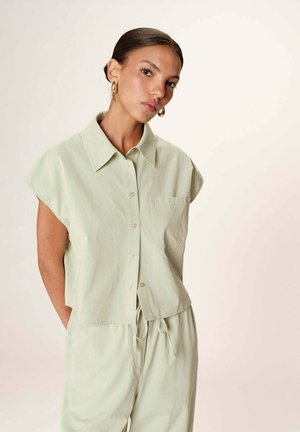 Chemise boutons à manches courtes vert clair avec col et poche, fabriquée en tissu doux, associée à un pantalon à cordon assorti.