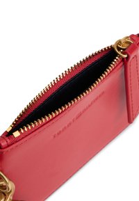 Portafoglio in pelle rossa con cerniera dorata, fodera interna nera e marchio in rilievo. Presenta una forma rettangolare e un moschettone staccabile.