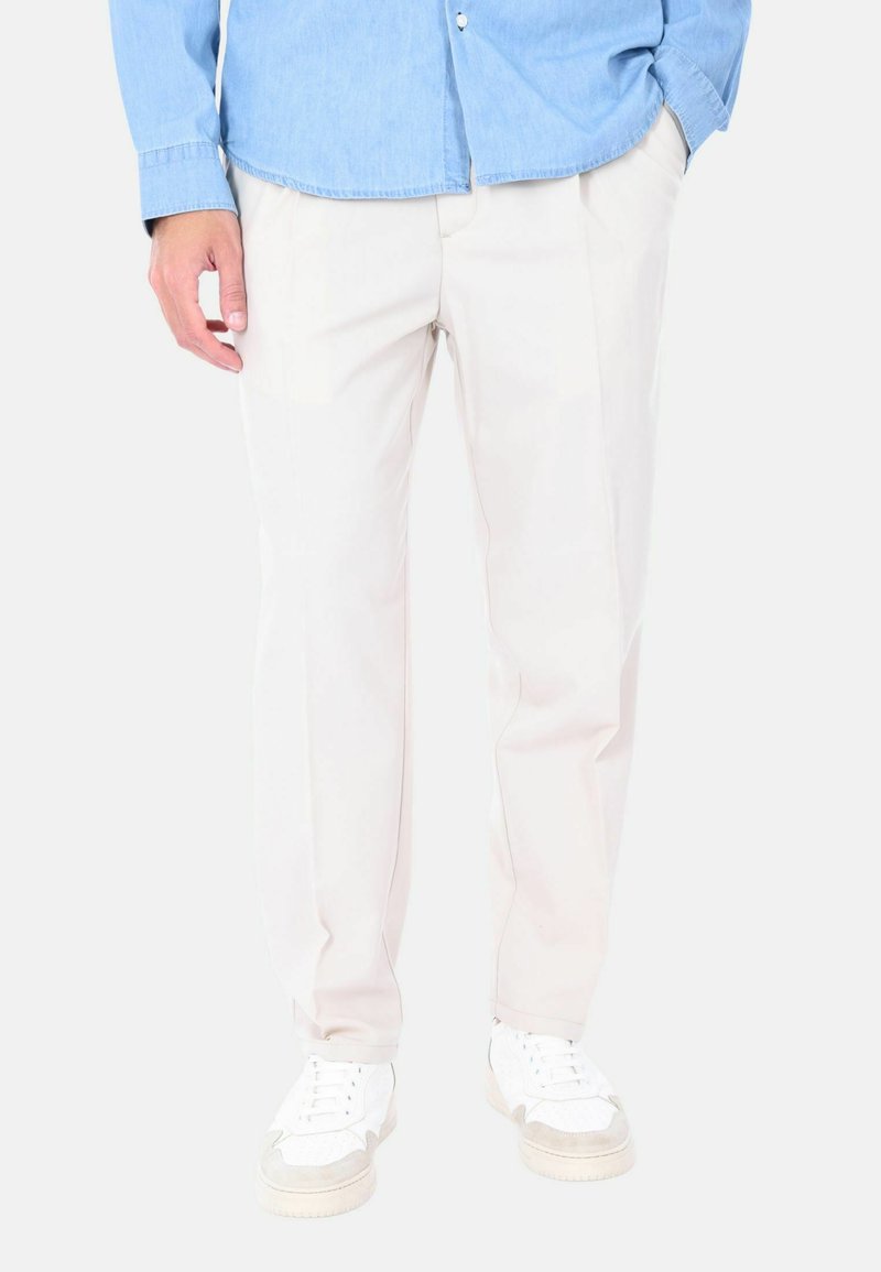 Pantaloni chiari, su misura, realizzati in un tessuto liscio, con un design a gamba dritta e tasche laterali, abbinati a sneaker bianche.