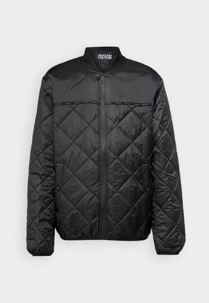 Veste doudoune noire matelassée avec un col rond, fermeture éclair à l'avant et motif en losange. Elle présente une texture lisse et des boutons-pression sur les côtés.