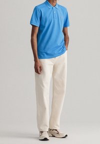 Polo bleu clair à col et manches courtes, associé à un pantalon droit couleur crème et des baskets beiges.