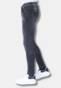 Strakke zwarte spijkerbroek van denim met subtiele vervaging, verweerde accenten en twee achterzakken, gecombineerd met witte sneakers met zwarte details.