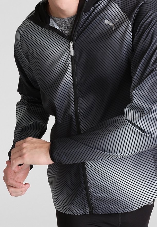 Giacca sportiva a strisce nera e grigia con chiusura a zip, dotata di cappuccio e realizzata in materiale liscio e leggero. Logo in alto a sinistra.