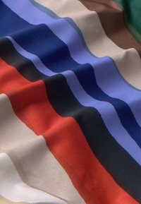 Kleurrijke stof met golvende strepen in rood, donkerblauw, lichtblauw, groen, bruin en beige, met een gladde textuur en glans.