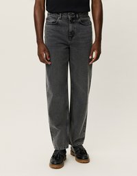 Melni platajās kājas džinsi, izgatavoti no denima, ar augstu jostu, kontrastējošu šuvju un priekšējām kabatām. Apvienoti ar melnām kurpēm.