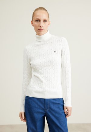 White cable-knit turtleneck sweater featuring ribbed cuffs and hem. The material appears soft, with a subtle logo detail on the chest.