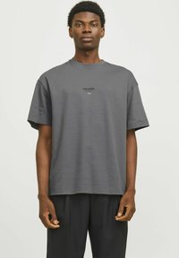 Grå bomulds t-shirt med løs pasform, korte ærmer og rund halsudskæring. Har trykt tekst "ESS.WRD." på brystområdet.