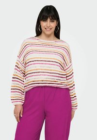 Pullover in crochet con motivo a righe orizzontali rosa, arancione e marrone su base crema; abbinato a pantaloni magenta fluidi e a coste.
