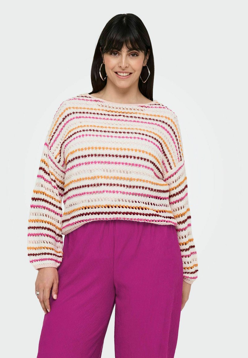 Pullover in crochet con motivo a righe orizzontali rosa, arancione e marrone su base crema; abbinato a pantaloni magenta fluidi e a coste.