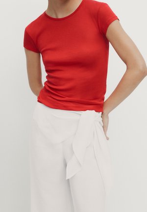 Person wearing a fitted red short-sleeve top and white high-waisted pants with a large front knot detail.