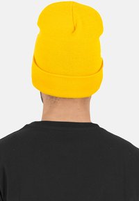 Yellow knit beanie with a folded cuff and a rounded top. Soft texture; simple, unembellished design. Worn with a black shirt.