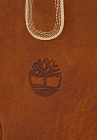 Ruskean nahkapinta, jossa on kohokuvioitu puu-logo ja valkoinen ommeltu nahkareuna.