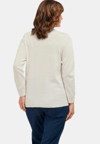 Helles beiges Sweatshirt mit langen Ärmeln, gerippten Bündchen und Saum sowie einer glatten Textur. Kombiniert mit dunkelblauen Jeans in lässiger Passform.