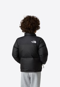 Svart dunjakke med høy krage og elastiske mansjetter, med et strukturert, polstret design. Logo vist på øvre del av ryggen.