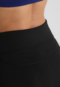 Czarne legginsy z wysokim stanem, wykonane z gładkiego, elastycznego materiału, z płaskimi szwami i szerokim pasem w talii dla komfortu i wsparcia.