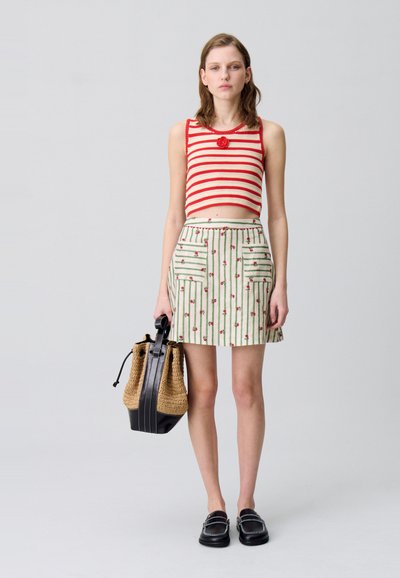 Top corto a righe rosse e bianche, gonna verde con motivi floreali, tasche e borsa a tracolla nera e intrecciata. Scarpe slip-on nere.