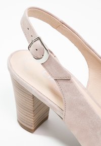 Chaussure à talon haut beige en daim à bride arrière avec boucle argentée et talon bloc en bois empilé sur fond blanc.