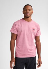 Helles rosa T-Shirt mit kurzem Arm, aus weichem Stoff, mit einer Brusttasche, die ein grafisches Design von Sonne und Welle zeigt. Runder Ausschnitt.