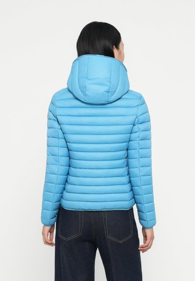 Veste matelassée bleu clair avec un motif cousu horizontal, capuche attachée et poignets élastiques. Portée sur un jean en denim foncé, vue de dos.