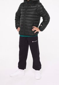 Czarna kurtka puchowa na zamek, z kapturem i poziomym przeszyciem. Dopasowana do czarnych spodni dresowych i białych sneakersów.