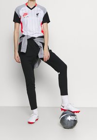 Koszulka Nike Liverpool FC w kolorach szarym, czarnym i czerwonym z pionowymi paskami. Czarne spodnie dresowe, białe skarpetki oraz korki z czerwonymi detalami. Piłka nożna Nike.