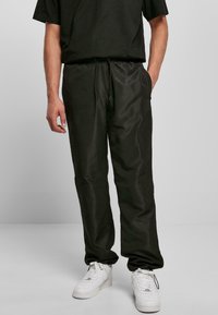 Pantalones negros ligeros con cordón, de textura suave, combinados con zapatillas blancas. El diseño incluye bolsillos laterales y un corte relajado.