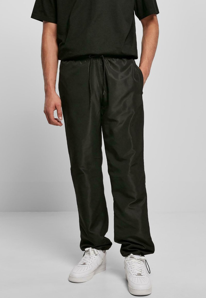 Pantalones negros ligeros con cordón, de textura suave, combinados con zapatillas blancas. El diseño incluye bolsillos laterales y un corte relajado.