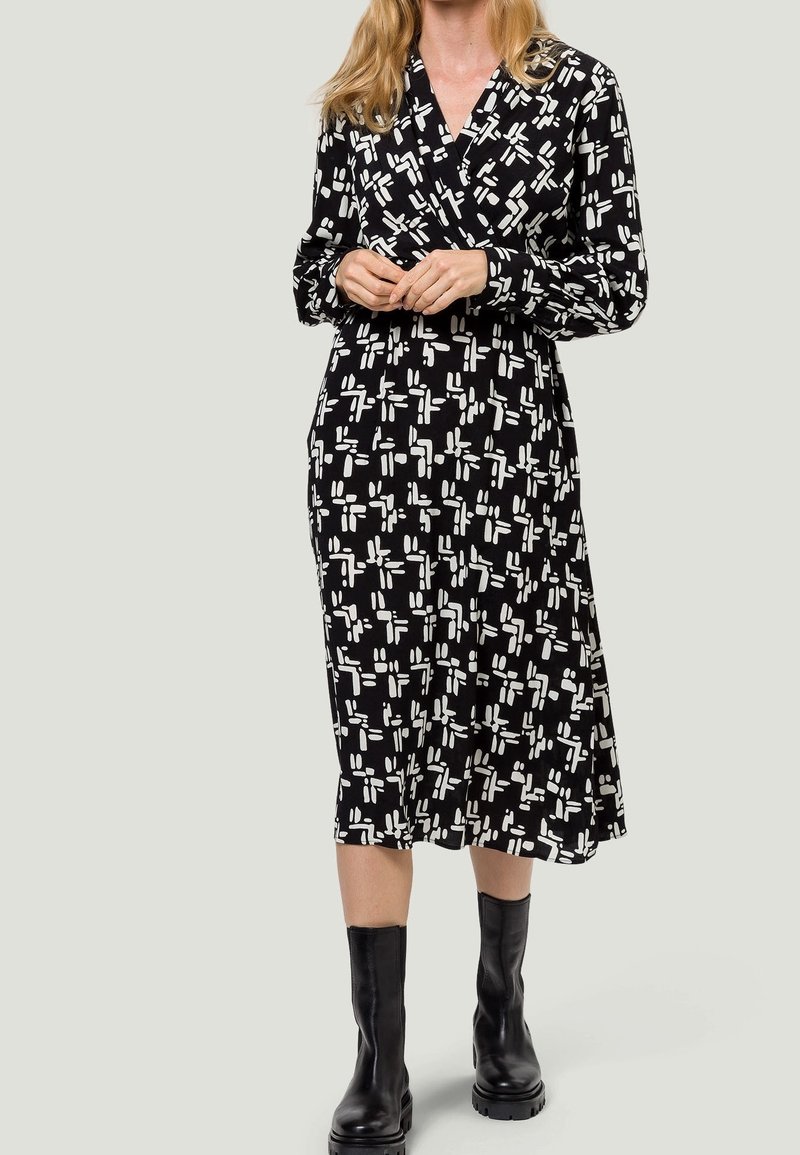 Robe midi noire avec un motif abstrait blanc, à manches longues et à col. Le tissu semble léger avec une texture lisse.