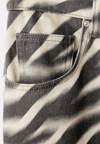 Tissu en denim rayé noir et blanc imitant les zébrures, montrant une poche avant avec des coutures visibles et un rivet en métal sur la ceinture.