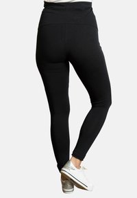 Leggings negros con una cintura alta, textura suave y un diseño ajustado. Combinados con zapatillas blancas con acentos plateados.