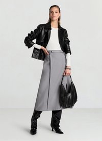 Veste en cuir noire portée sur un haut blanc, jupe longue grise avec un pli sur le devant, et bottes noires brillantes montant jusqu'aux genoux. Sac à main noir avec franges.