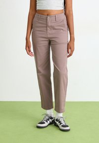 Lichtbruine chino's van katoen met een rechte pasvorm. Voorzien van voor- en achterzakken, gecombineerd met zwart-witte sneakers en witte sokken.