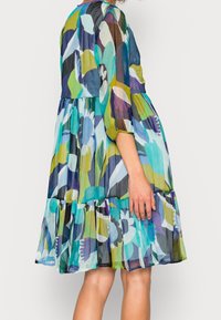 Barevné, vrstvené midi šaty s třičtvrtinovými rukávy. Průhledná látka je zdobena abstraktními květinovými vzory v modrých, zelených a fialových odstínech.