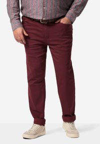Chinos burdeos con un corte recto, fabricados con una mezcla de algodón, que cuentan con bolsillos frontales y puños enrollados. Combinados con zapatillas de color claro.