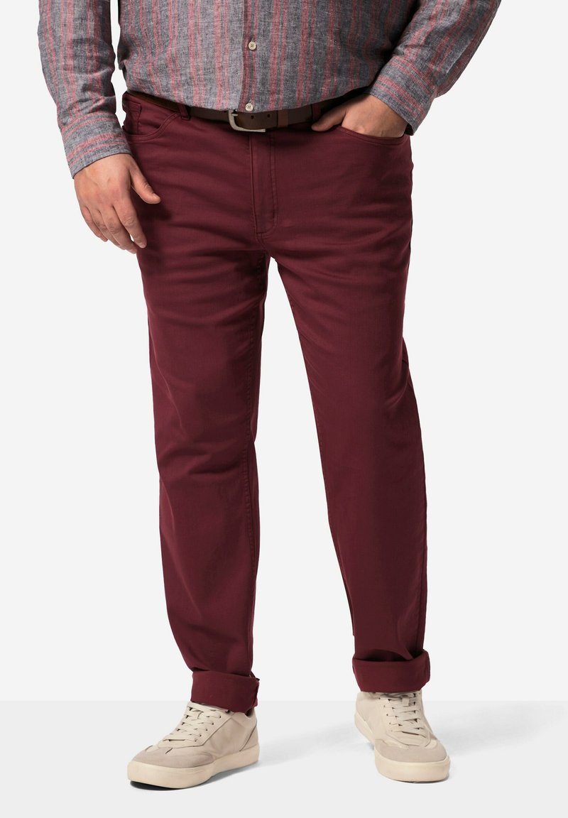 Chinos burdeos con un corte recto, fabricados con una mezcla de algodón, que cuentan con bolsillos frontales y puños enrollados. Combinados con zapatillas de color claro.