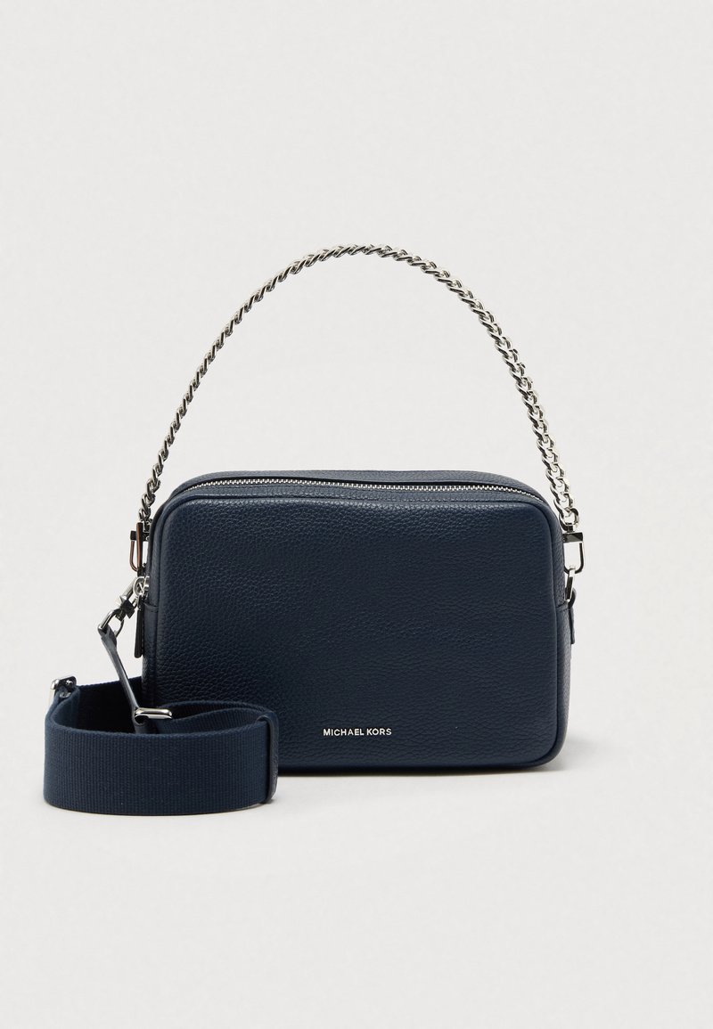 Tamnoplava kožna torba na rame s teksturiranim završetkom, lancem za nošenje i odvojivim platnenim remenom. Ima zatvarač na patentni zatvarač i detalj s logotipom.