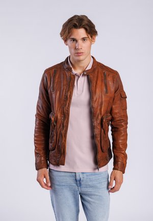 Bruine leren jas met een getailleerd ontwerp, ritszakken en geribde mouwen. Draagt over een lichtroze polo en blauwe spijkerbroek.