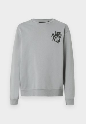 Svetlo siva majica s kapuljačom, izdelana iz mehkega blaga, z okroglo ovratnico in dolgimi rokavi. Črn grafični napis na levem prsnem delu.