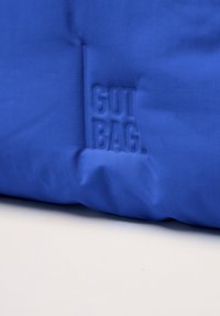Niebieski worek ze sznurkiem, o gładkiej fakturze, z wytłoczonym logo "GOT BAG" na boku. Prosty, funkcjonalny design.