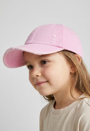 Young girl with light brown hair wearing a pink baseball cap and beige shirt, looking slightly to the side with a soft smile.