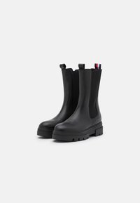 Botas Chelsea de cuero negro con paneles laterales elásticos y tiradores, que presentan una suela de goma gruesa y un diseño minimalista.