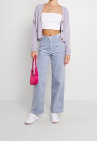 Světle fialový pletený cardigan s knoflíky, bílý crop top, světle modré široké kordové kalhoty, růžová kabelka a bílé tenisky s akcenty.