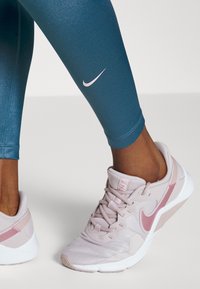 Leggings teal avec un logo swoosh Nike rose et une coupe ajustée. Chaussures de sport rose pâle avec un dessus texturé et une semelle blanche.