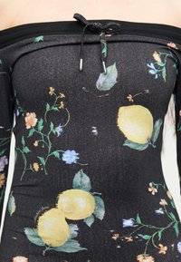 Μαύρο τοπ με ακάλυπτους ώμους και κορδόνι στο λαιμό, διακοσμημένο με κίτρινα λεμόνια, πράσινα φύλλα και μικρά πορτοκαλί και μπλε λουλούδια.