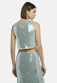 Geknipte mouwloze top van glinsterende stof in lichtblauw, met een sleutelgatdetail aan de achterkant en een zachte textuur.