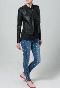 Veste de moto en cuir noir sur une chemise noire, associée à un jean skinny bleu à motifs d'étoiles et des chaussures roses avec une semelle réfléchissante.